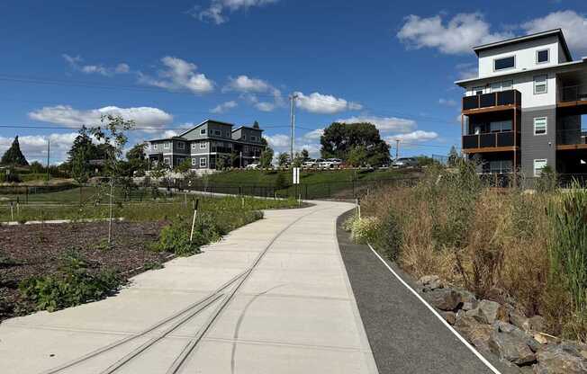 A path runs through a grassy area of Claggett Creek Park with Verda Crossing Apartments in the background.