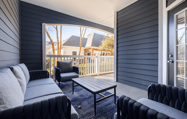 A black couch sits in a living room with a view of a deck and trees outside.