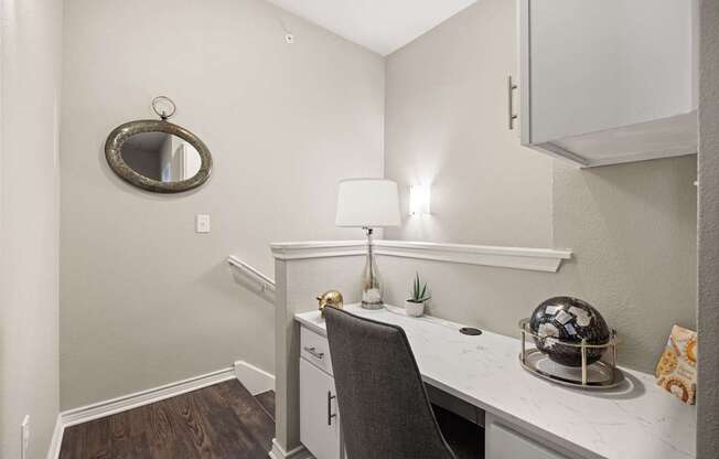 A white desk with a chair and a mirror on the wall.
