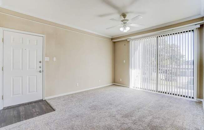Entrance view of the living area at Saxony at Chase Oaks Apartments in Dallas, TX, showing beige walls, a white front door, and large windows with vertical blinds.
