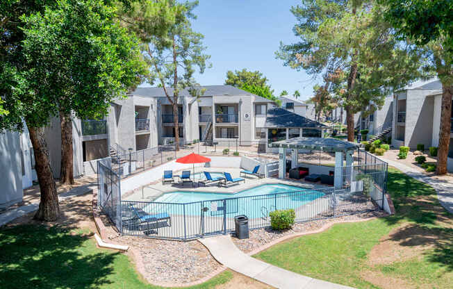 A swimming pool surrounded by a fence and trees in a residential area.
