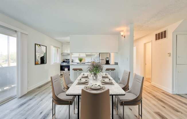 a dining area with a long table and chairs and a kitchen in the background