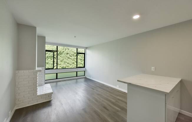 an empty living room with a kitchen and a window