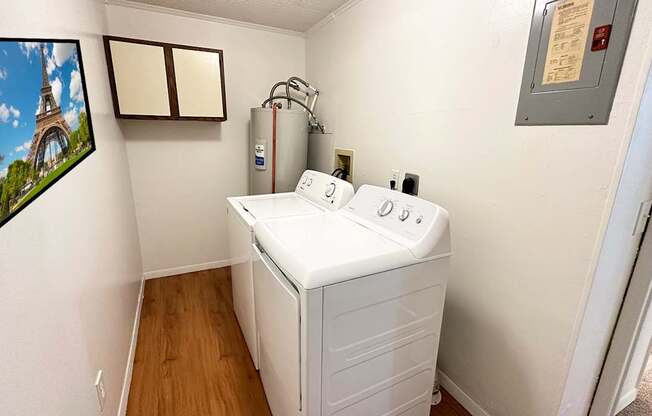 A washing machine is in a small room with a picture of the Eiffel Tower on the wall.