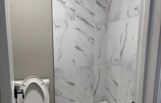 A white toilet with a white tank is in a bathroom with a marble tile wall.