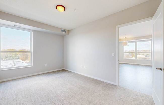 A spacious, empty room with a large window and a door leading to another room.