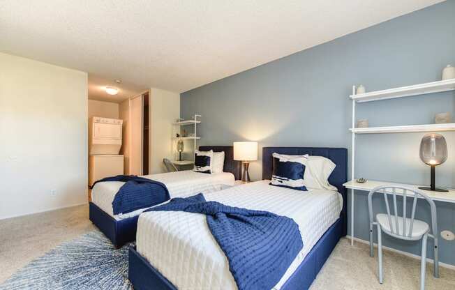 Model home bedroom with two beds and a desk with a chair. Stackable washer and dryer inside room at Renaissance Park Apartments, Davis, California