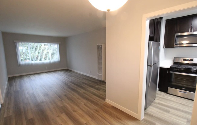 an empty living room with a kitchen in the background