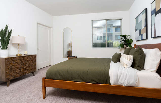 A bedroom with a bed, nightstand, and a plant.