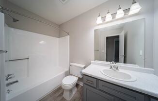 modern bathroom with tub, sink, toilet, mirror, and light