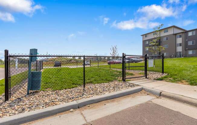 A black fence surrounds a green trash can next to a sidewalk.