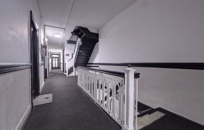 a long hallway with stairs and white walls and a black staircase