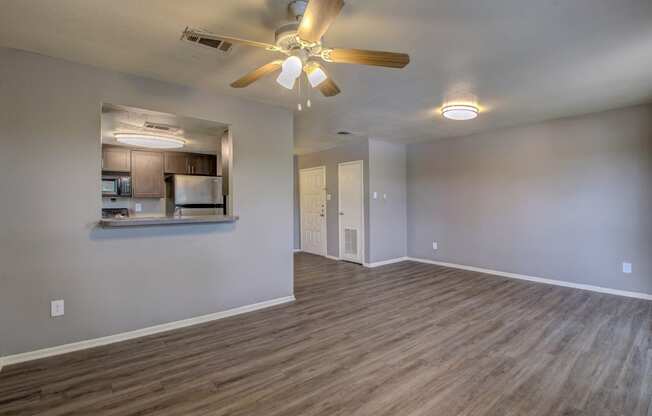 an empty living room with a ceiling fan and a kitchen