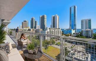 A woman is sitting on a balcony with a view of a city skyline.