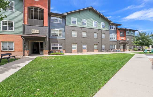 a sidewalk in front of an apartment building with a lawn at Switchback on Platte Apartments, Littleton, CO