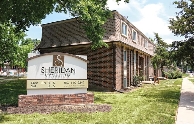 A sign for Sheridan Crossing is in front of a brick building.