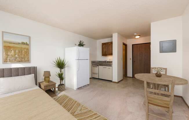 Mandan, ND Garden Grove Apartments. A bedroom area in a studio with a bed a table and a chair and a refrigerator