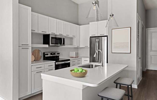A kitchen with white cabinets and appliances, a bowl of fruit on the island, and a picture frame on the wall.