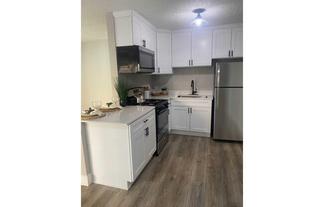 Modern kitchen featuring white cabinets, stainless steel appliances, and a sleek countertop. The layout includes a stove, microwave, sink, and refrigerator. Soft lighting illuminates the space, complemented by a stylish wooden floor and decorative items on the counter.