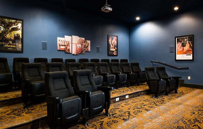 A row of black theater seats with a carpeted floor and posters on the wall.