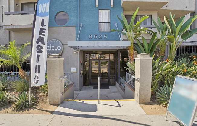 A blue building with a sign that says "NOW LEASING" in front of it.