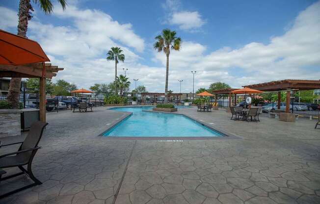 A pool surrounded by palm trees and a patio area at Willow Creek Apartments, Texas, 77012