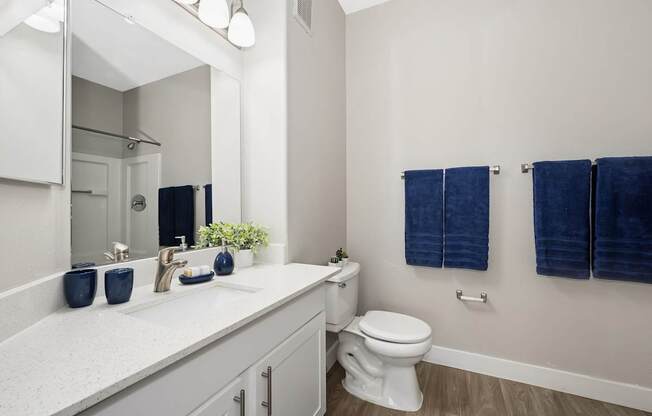 A white bathroom with a toilet, sink, and blue towels.