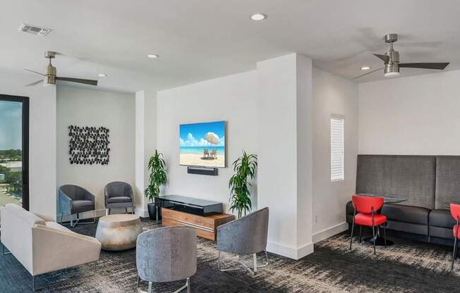 A living room with a grey couch, red chairs, and a painting of a beach scene on the wall.