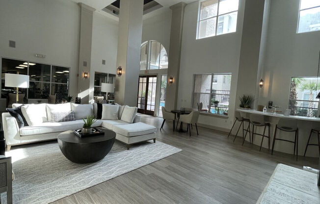 A spacious living room with a large white sofa, a coffee table, and a bar area with stools.