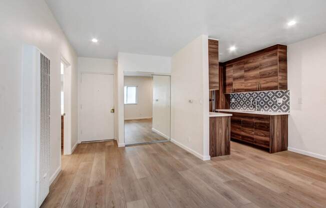 a living room with white walls and wooden floors and a kitchen with a wooden cabinet