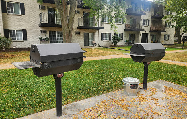 Two mailboxes are on a concrete slab with a tree and apartment building in the background.
