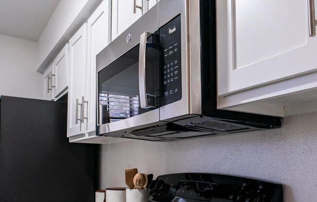 A black microwave oven mounted above a black stove in a kitchen.