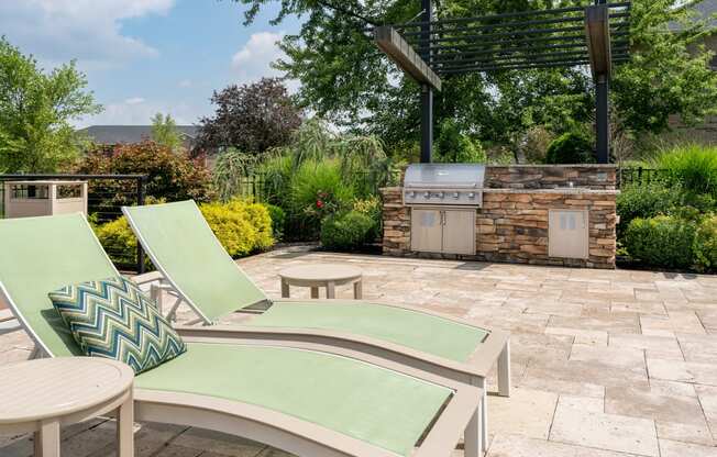a patio with a grill and two lounge chairs