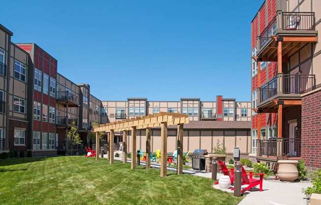A sunny day at a modern apartment complex with a grassy area and a wooden pergola.