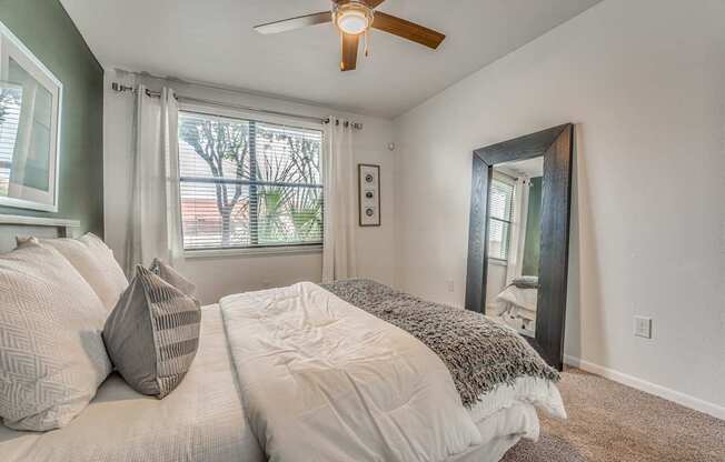 A bedroom with a bed, pillows, a ceiling fan, and a window with curtains.