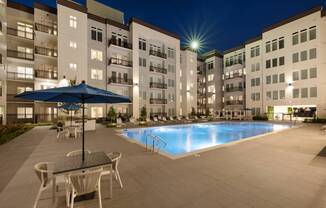 a swimming pool at night with an umbrella in front of an apartment building