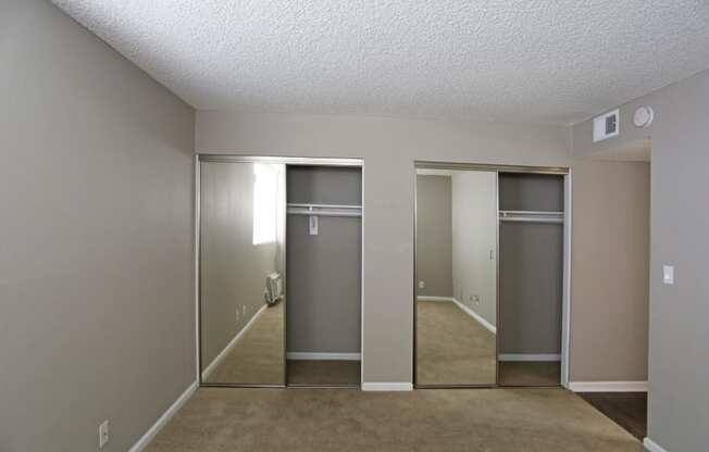 A room with a carpeted floor and two closets with mirrors.