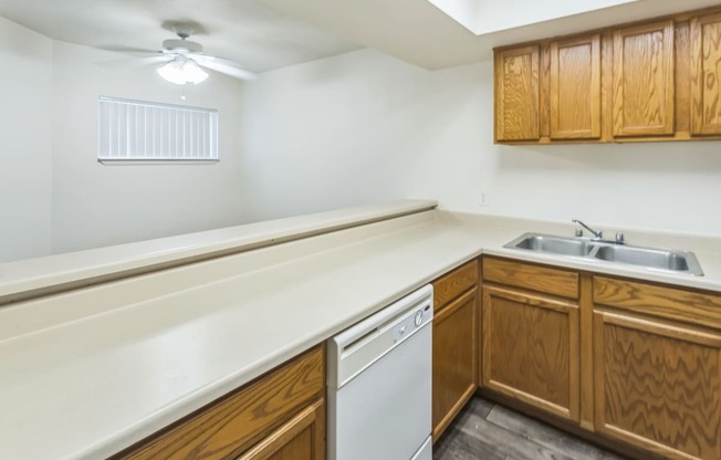 an empty kitchen with wooden cabinets and a white dishwasher and sink