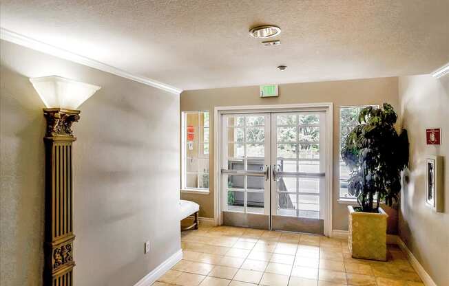 A hallway with a plant in a planter, a door with a glass panel and a fire extinguisher on the wall.