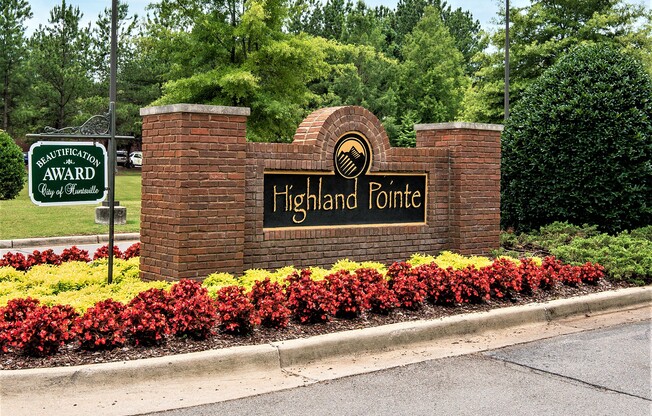 a brick monument sign for highland pointe with red and yellow flowers in front of it