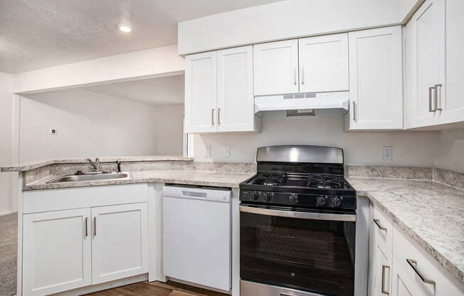A kitchen with a gas stove, dishwasher, and white cabinets at West Hampton Park Apartments in Elkhorn, NE 68022