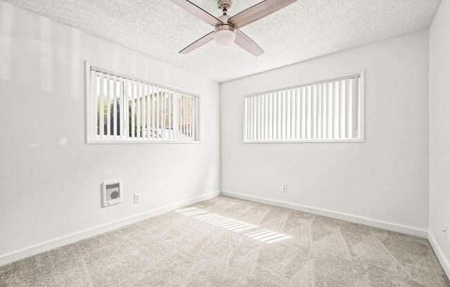 an empty room with a ceiling fan and two windows