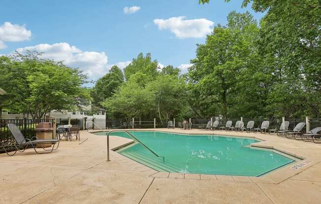 A pool surrounded by trees and chairs.