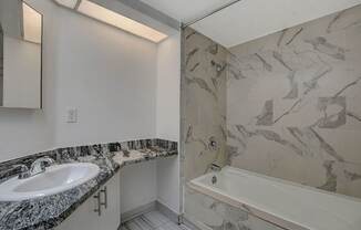 A bathroom with a marble patterned shower and a white sink.