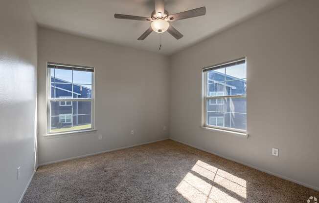 A room with a ceiling fan and two windows.
