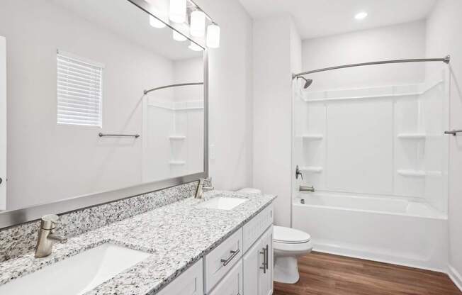 A white bathroom with a granite counter top and a walk-in shower.