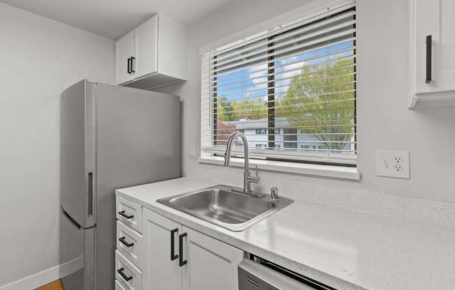 A kitchen with a refrigerator, sink, and window.