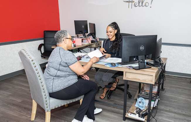 two women sitting at a desk in front of a computer