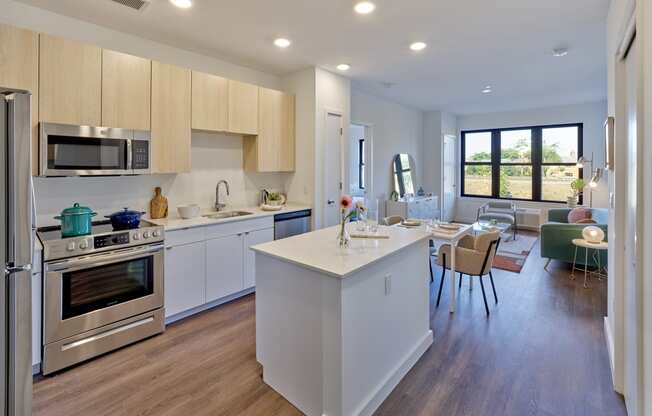 Bright kitchen and living room with an open floor plan at The Mint Rahway, featuring modern appliances, a central island, and large windows, perfect for studio apartments near Newark Airport.