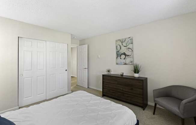 A Spacious Bedroom with a White Bed and a Brown Dresser Beside Two Large White Closet Doors at Pacific Park Apartment Homes, Washington